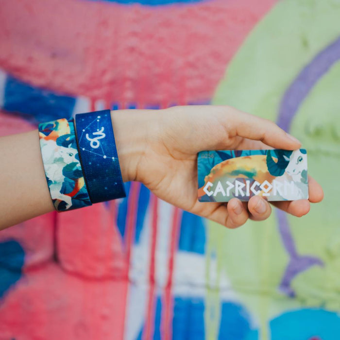 Close up image of hand holding a card with Capricorn on it and two Capricorn straps on their wrist