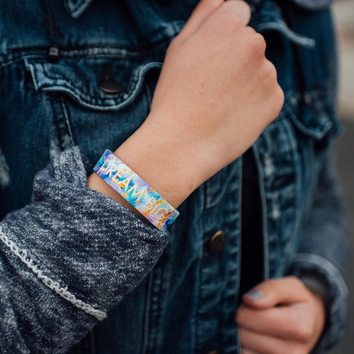Lifestyle photo up close of wrist while wearing dream big single showing inside design with dream big in bold text with blue, purple, and yellow watercolored background