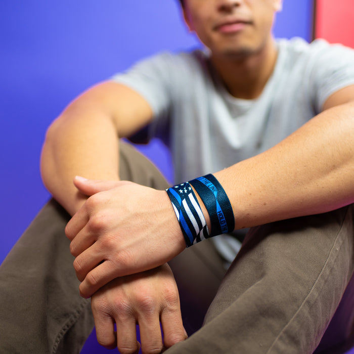 Studio image of sitting model with arms crossed in front of their knees and 2 Hold The Line on their wrist