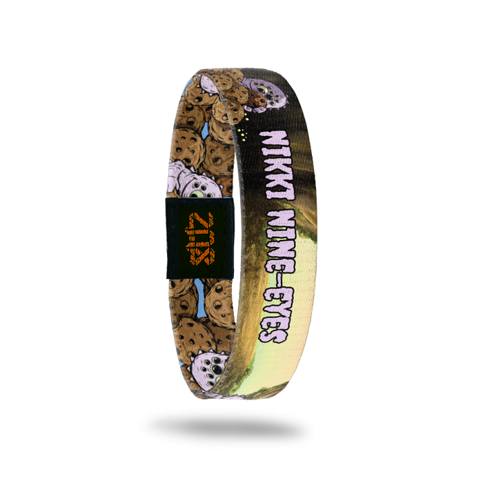 Product photo of the inside of 2020 - Day 7 - Nikki Nine-Eyes: cave design light purple monster with 9 eyes and spikes on back holding a cookie with light purple "NIKKI NINE-EYES" text