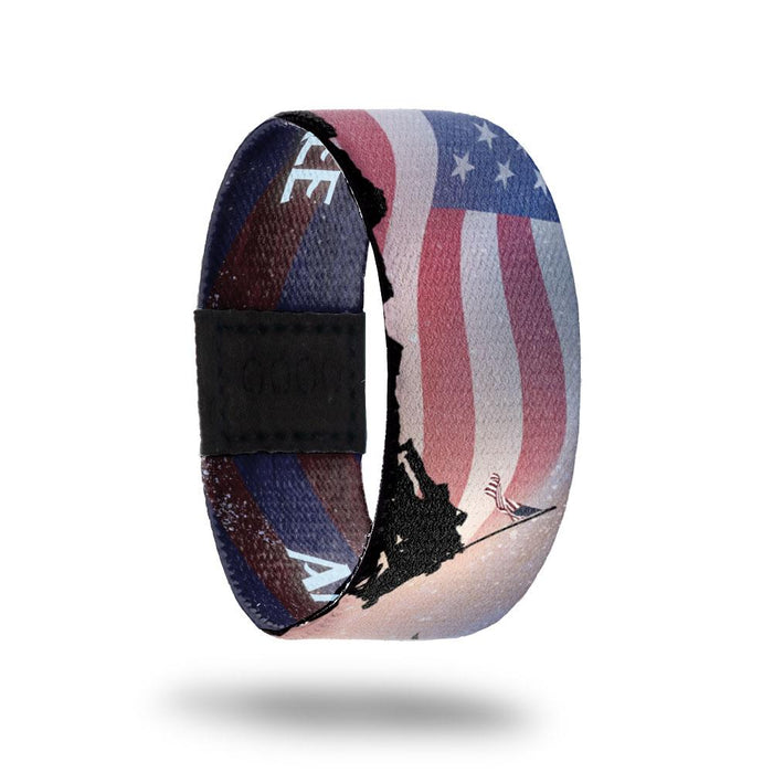 Outside design of America, The Free: United States flag in the background with faded color and black silhouette of soldiers raising a flag on a slanted pole