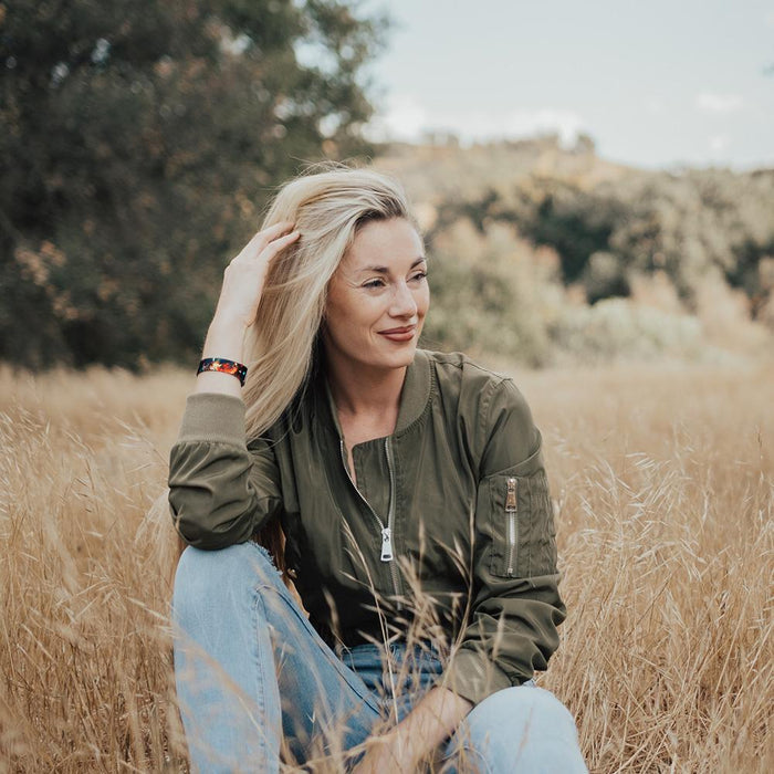 Lifestyle image of someone smiling and sitting in a field with Anything Is Possible on their wrist