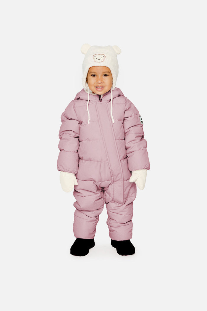 Baby standing in the lavender Deux par Deux Baby Cloud snowsuit with a cream bear hat and mittens, front view