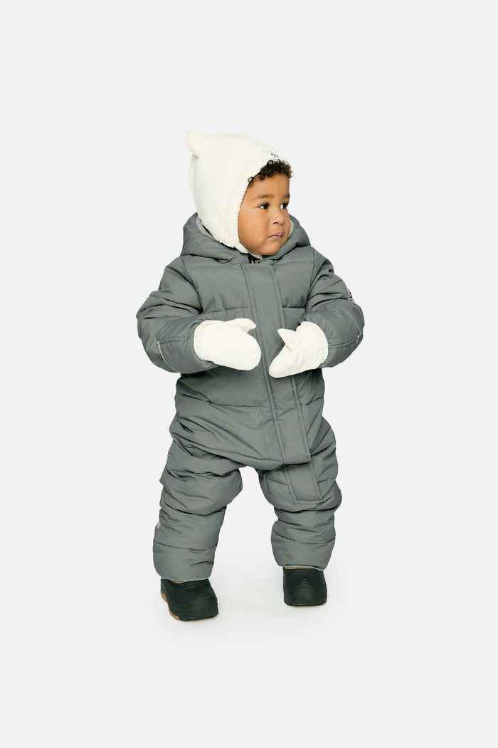 Baby standing in the sage green Deux par Deux Baby Cloud snowsuit with cream mittens, front view
