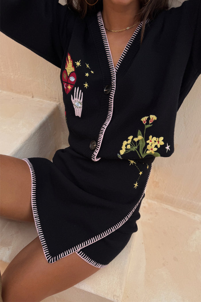 Black Night Garden Mini Wrap Skirt with pink blanket stitch trim and mystical heart, hand, and star motifs.