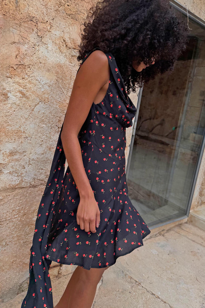 Black Rose Mini Sophie Dress featuring a red rose print, cowl neckline and draped scarf detail on a model.