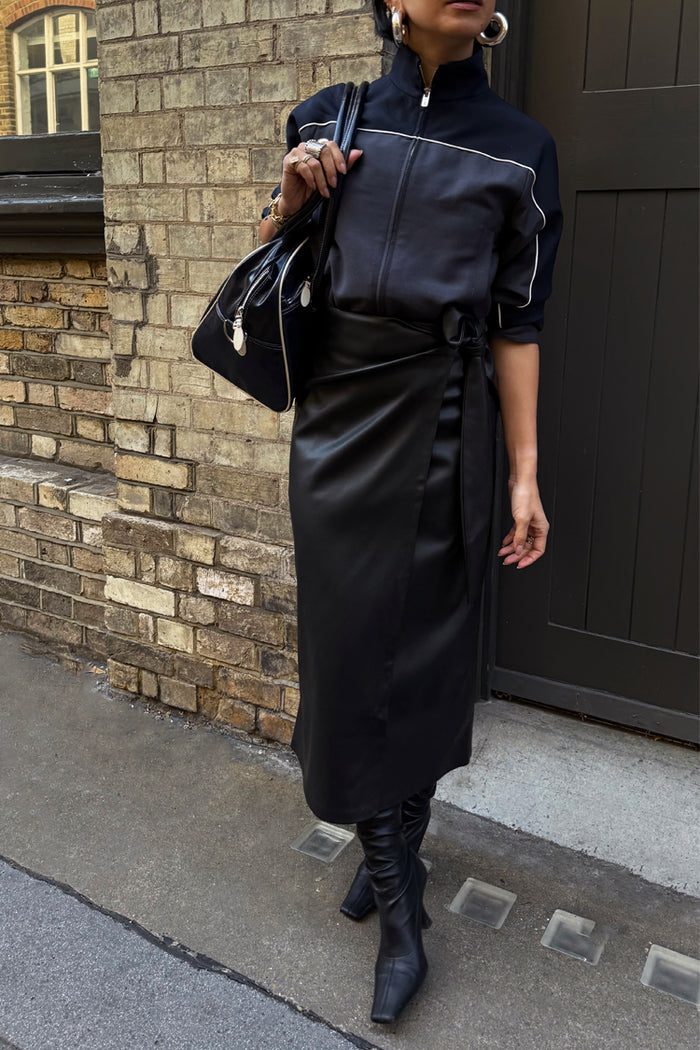 Black Vegan Leather Jaspre Wrap Skirt with a tulip tie, styled with a black zip jacket and boots.