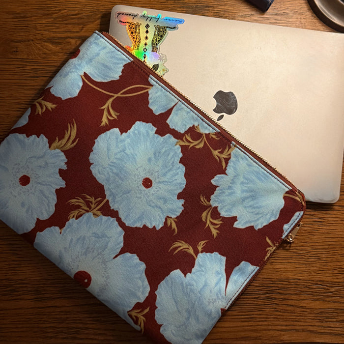 Blue and Burgundy Poppy Laptop Case with a large floral print and zip closure, holding a silver laptop on a wooden desk.