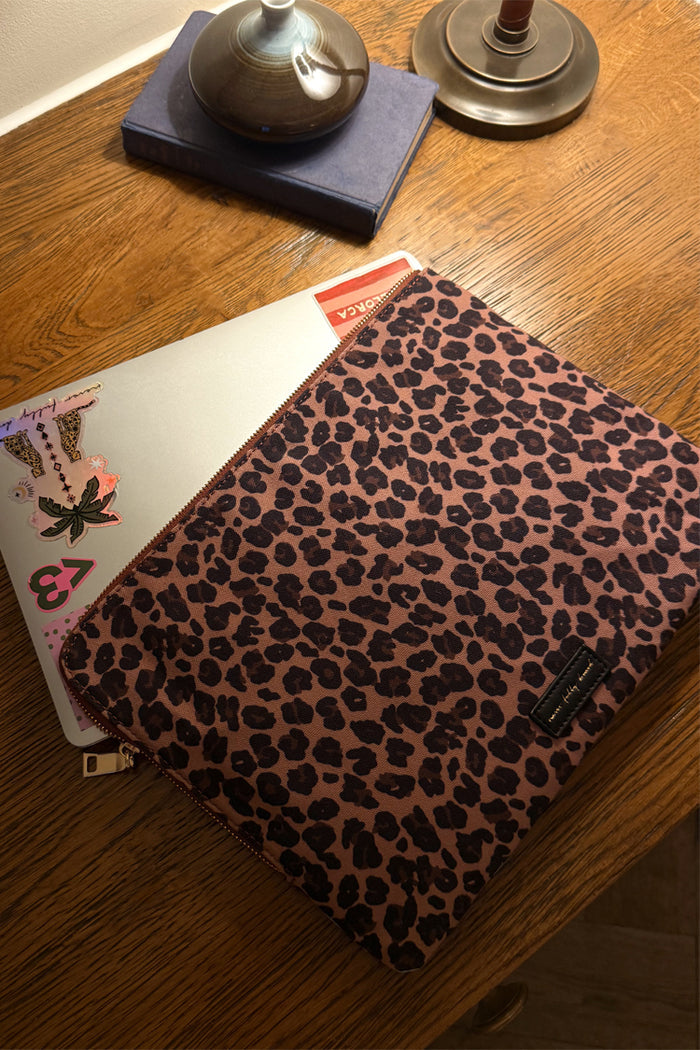 Reversible leopard print laptop case with a gold-tone zip, shown on a wooden desk with a silver laptop.