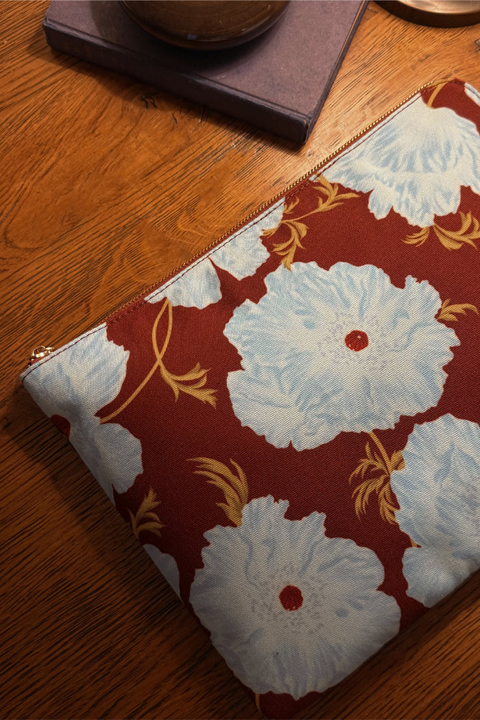 Blue and Burgundy Poppy Laptop Case featuring an in-house designed floral print and gold zip on a wooden table.