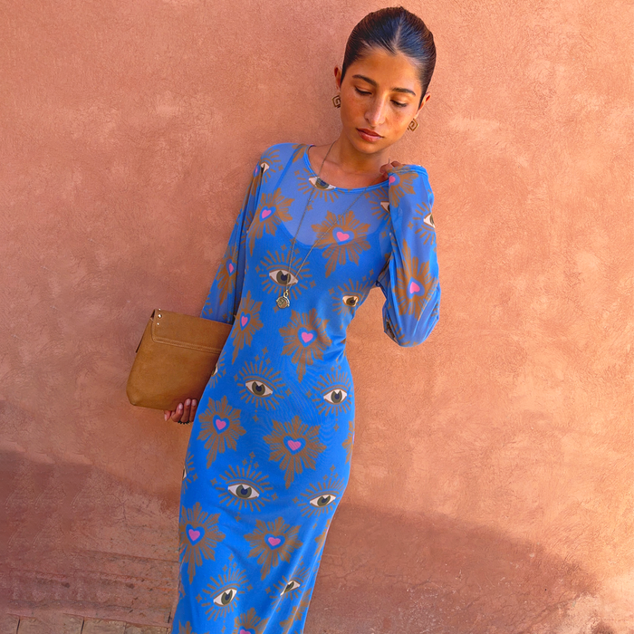 Blue Eye Mesh Dress Petite with heart and eye motifs on a stretch base, styled with a tan clutch against a terracotta wall.