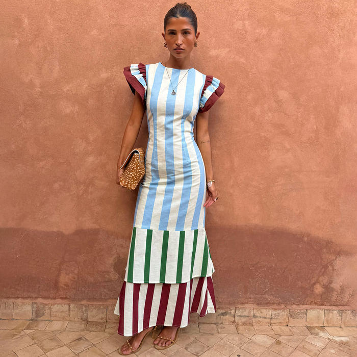Blue Stripe Alena Midi Dress with green and burgundy tiered panels and ruffle sleeves on a model by a terracotta wall.