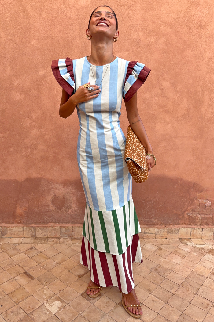 Blue Stripe Alena Midi Dress featuring ruffle sleeves and a multi-coloured tiered skirt against a textured wall.