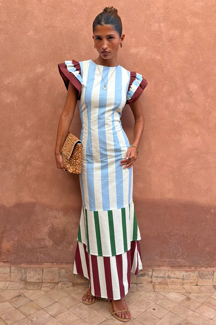 Blue Stripe Alena Midi Dress with tiered green and burgundy stripes and frill sleeves against a terracotta wall.