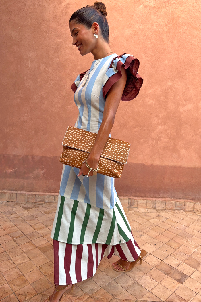 Blue Stripe Alena Midi Dress featuring tiered striped panels and burgundy ruffle sleeves, paired with a spotted clutch.