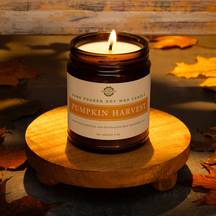 Rustic Strength, Candle, 8oz, Amber Glass, photoshoot image showing a lit candle on a wooden platform set in a rustic, warmly lit setting surrounded by fall leaves. Pumpkin Harvest scent