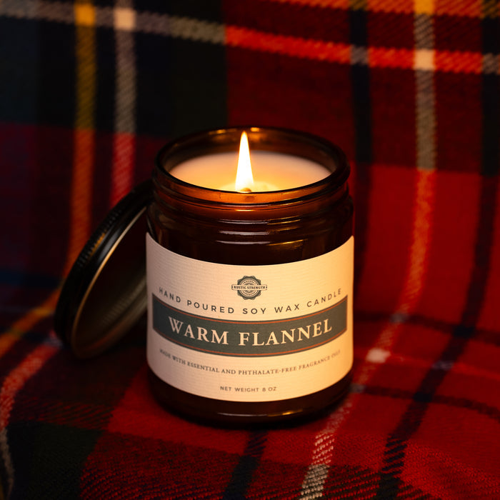 Rustic Strength, Candle, 8oz, Amber Glass, Warm Flannel, photoshoot image with lit candle set on a red-dominant plaid fabric