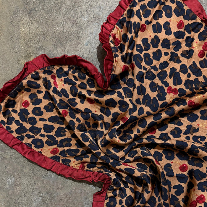 Cherry Leopard Bandana featuring a red ruffled border and cherry-patterned leopard print on a grey stone surface.