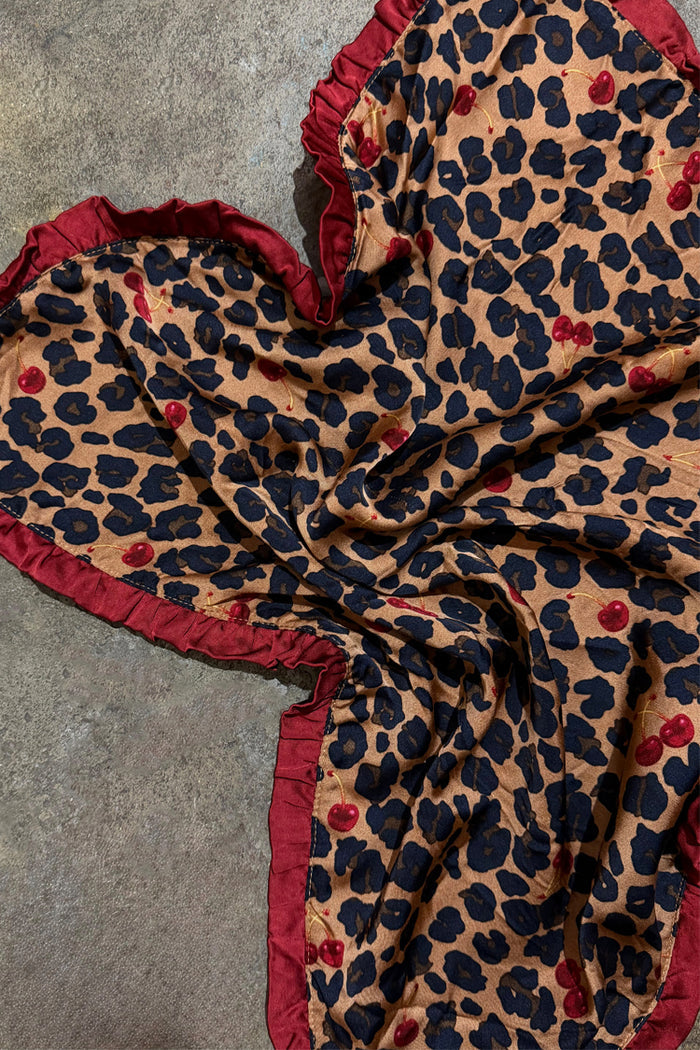 Cherry Leopard Bandana featuring leopard print with red cherries and a deep red ruffled border on a textured surface.