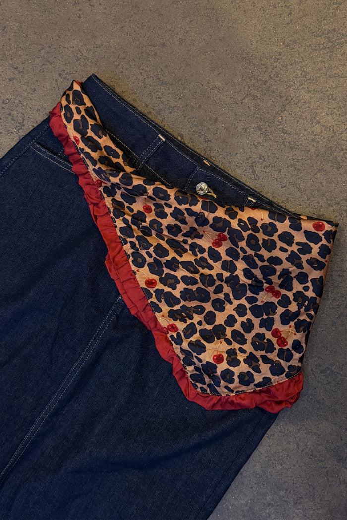 Multi-wear Cherry Leopard Bandana with a red ruffle border and cherry print, styled as a belt on dark denim.