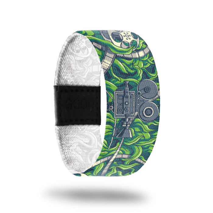 Outside design of Cinephile has a old film projector in gray at the center of the design with white and gray colored film unraveled along the design over a green grass-like background