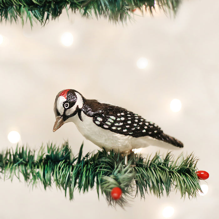 A small bird ornament with black and white markings and a red spot on its head sits on a green artificial pine branch with red berries, against a softly lit background.