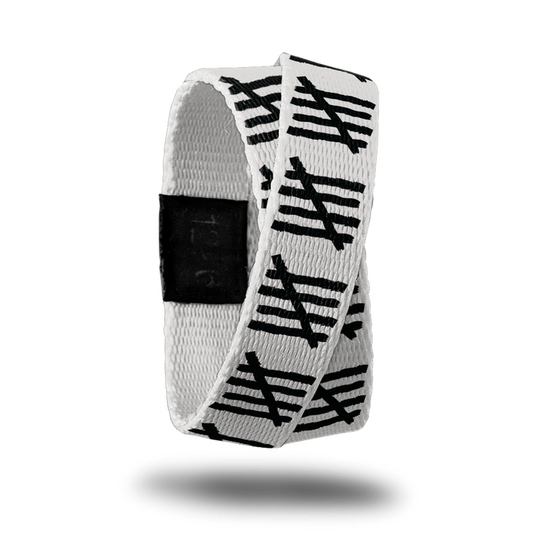 Outside design of Count You Blessings is a white-grey background with a repeated patten of the image of four black lines with one black line running diagonally across the four black lines. This product, called a double, is thinner and wraps around your wrist twice with the material crossing at one point.