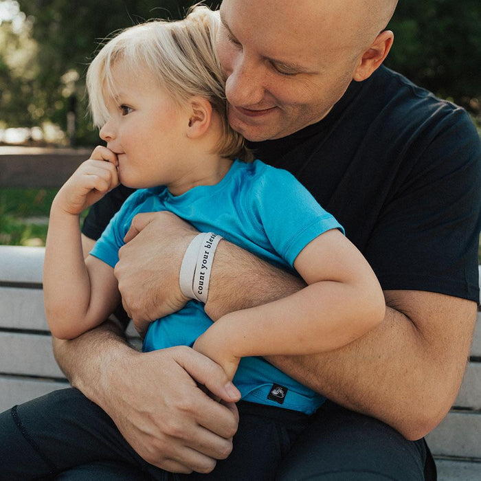 Lifestyle image of man hugging son with Count Your Blessings on his wrist