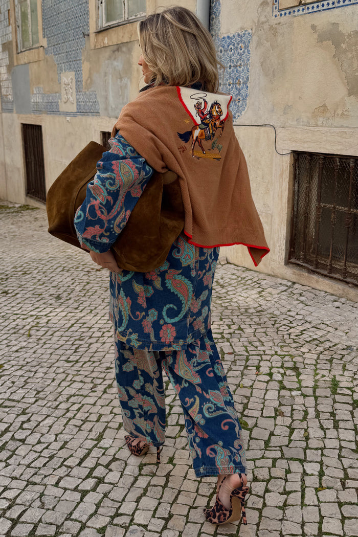 Tan brown Cowgirl Martha Cardigan with an embroidered western motif, draped over a paisley co-ord on a cobbled street.