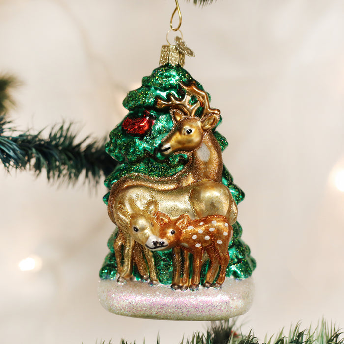 A Christmas tree ornament featuring a glittery green tree with two golden deer, one adult and one fawn, standing together in front, hanging on a branch.
