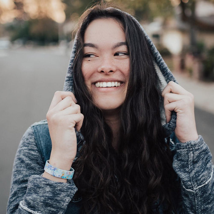 Lifestyle photo of girl grasping the hood of her jacket wearing dream big single showing outside design with a white geometric design overlaying a blue, purple, and yellow watercolored background