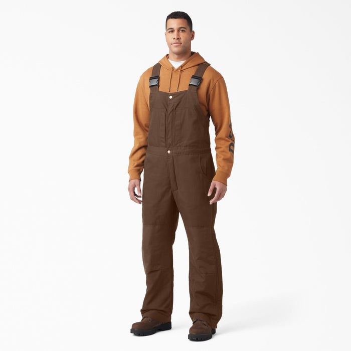 Man wearing brown insulated bib overalls with shoulder straps and orange hoodie underneath.