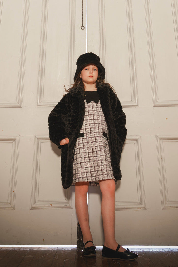 Girl standing in the Deux par Deux black faux fur long coat over a checked dress