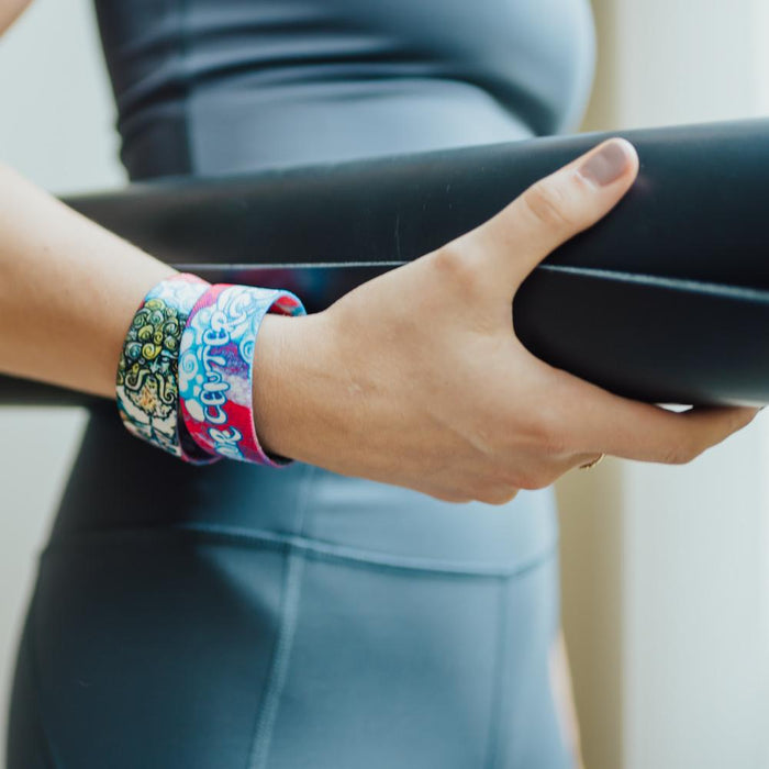 Lifestyle close up image of model holding a rolled up yoga mat and wearing two Find Your Center straps