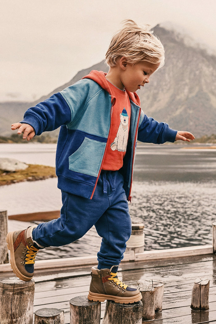 Boy jumping along a dock outdoors in the Deux par Deux blue, turquoise and orange fleece jacket