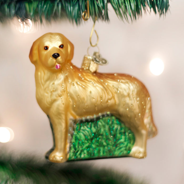 A golden retriever dog ornament with a small gift on its back hangs from a Christmas tree branch, with blurred lights in the background.