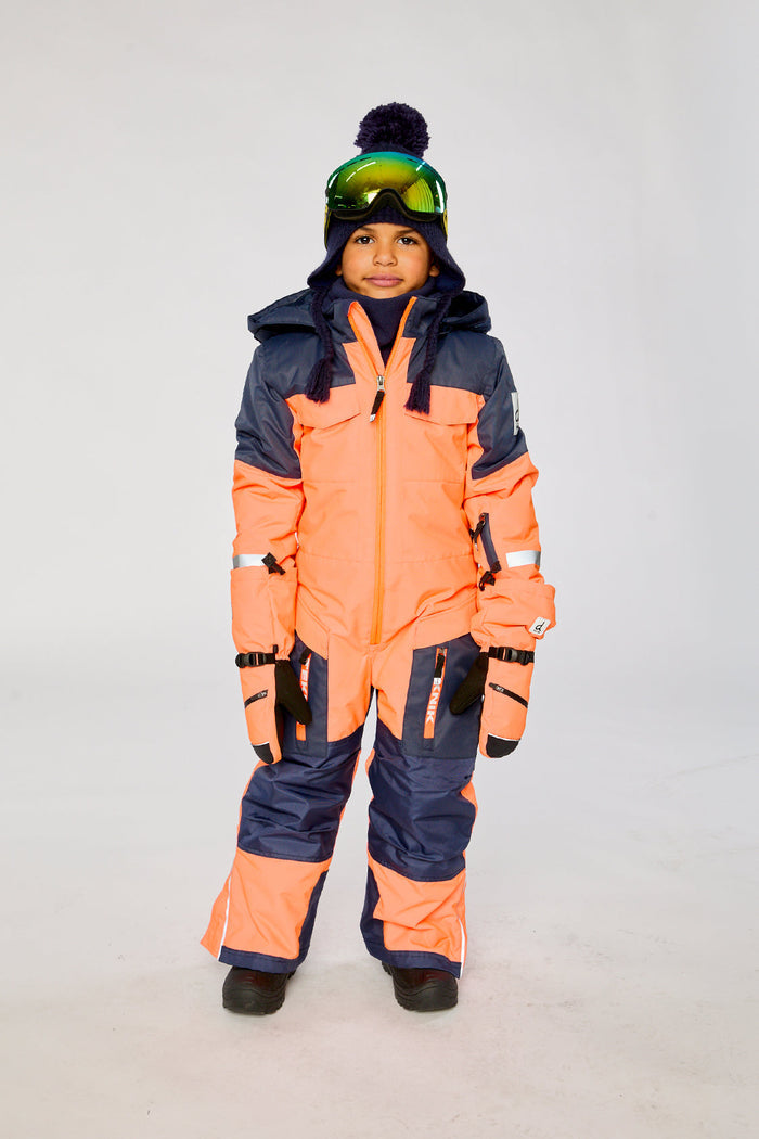 Child wearing the bright orange and blue Deux par Deux TEKNIK one-piece snowsuit with goggles, front view