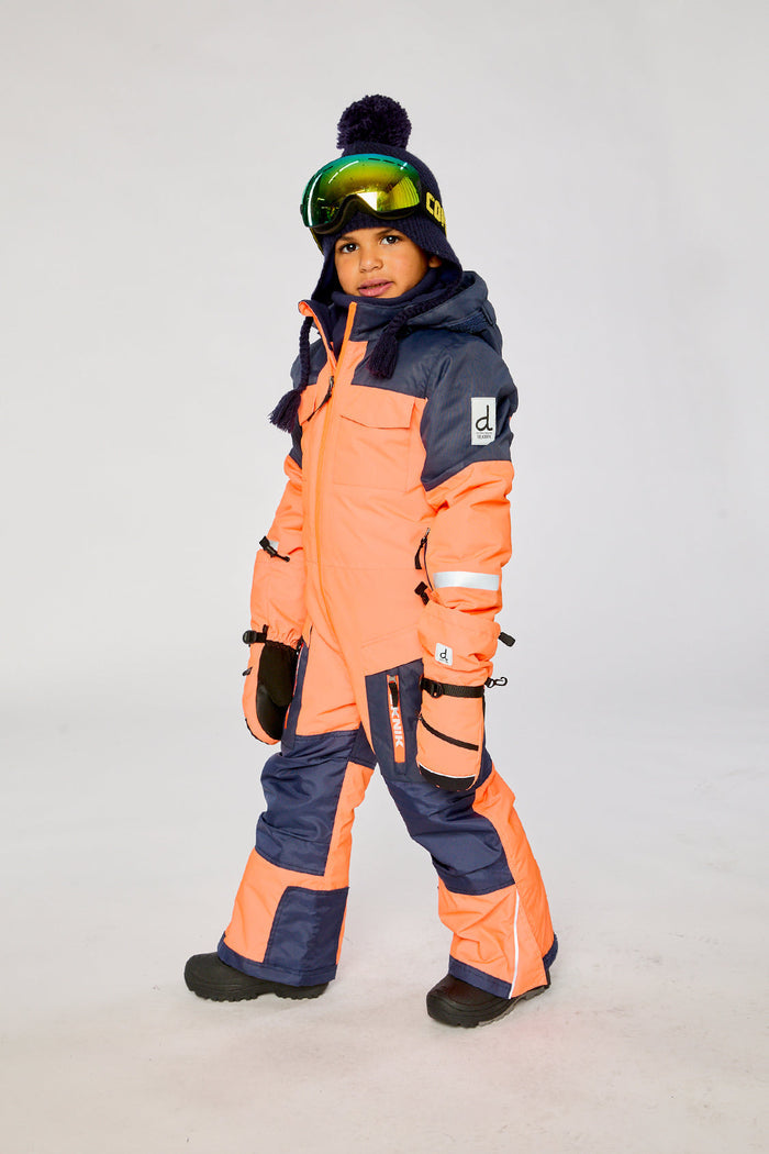Child wearing the bright orange and blue Deux par Deux TEKNIK one-piece snowsuit, side view