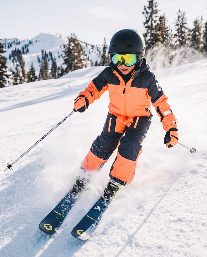 Child skiing downhill in the bright orange and blue Deux par Deux TEKNIK one-piece snowsuit