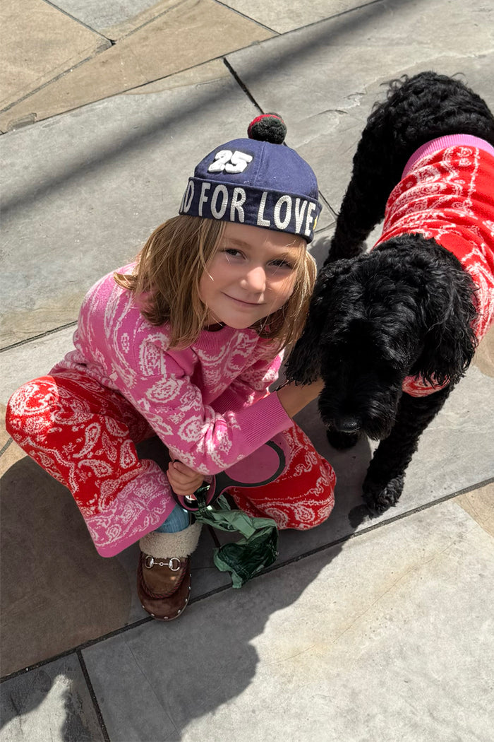 Kids Red and Pink Bandana Knitted Set worn by a child crouching next to a dog in a matching jumper.