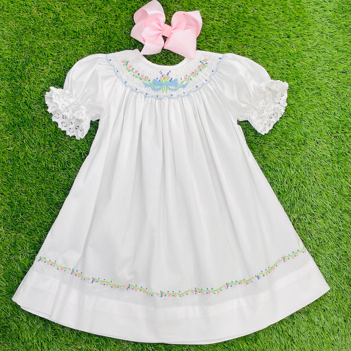 A white heirloom dress with short lace sleeves and multicolored embroidery around the hem and neckline