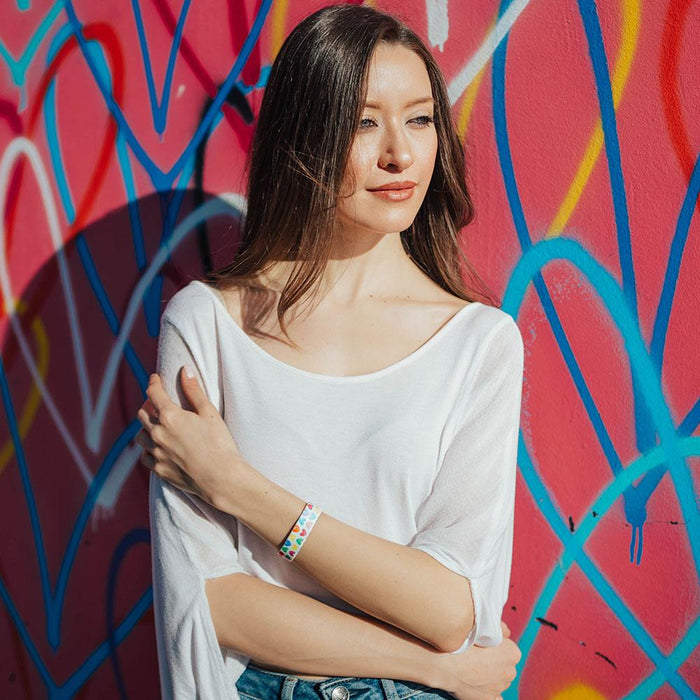 Lifestyle photo of girl with live with love single showing the outside design of with rows of pastel orange, yellow, pink, green, purple, and blue gradient hearts over white background