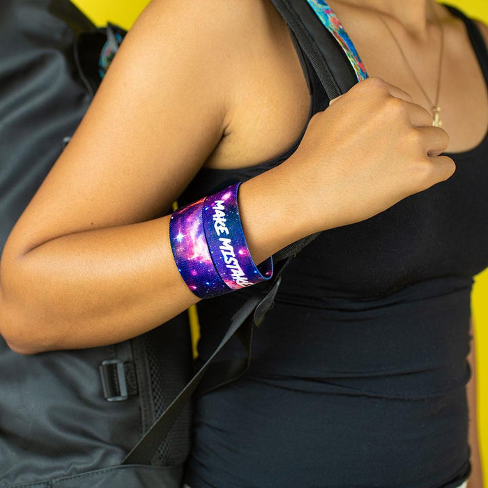 Studio close image of model holding backpack strap with 2 Make Mistakes on wrist
