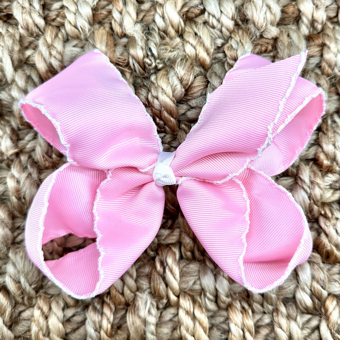 A light pink grosgrain ribbon hair bow with white scalloped edges
