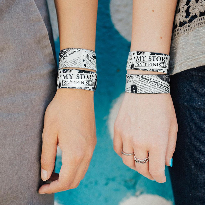 Lifestyle image close up image of two wrists both wearing 2 My Story Isn't Finished straps