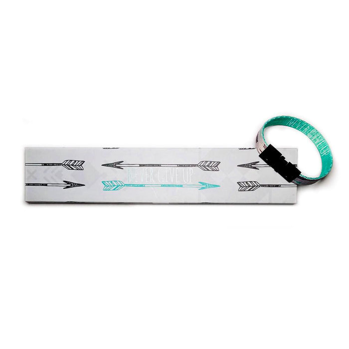 Studio image of Never Give Up clasped together laying on the box it comes in, which has a design of a grey background, black and teal-green illustrated arrows with Never Give Up in white text.