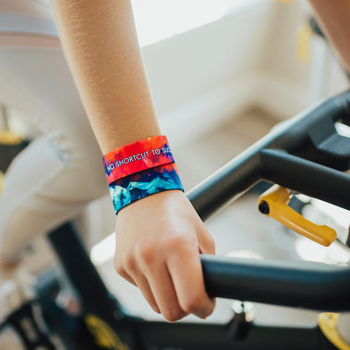 Lifestyle image of someone resting hands on an exercise bike with 2 No Shortcut To Success on wrist