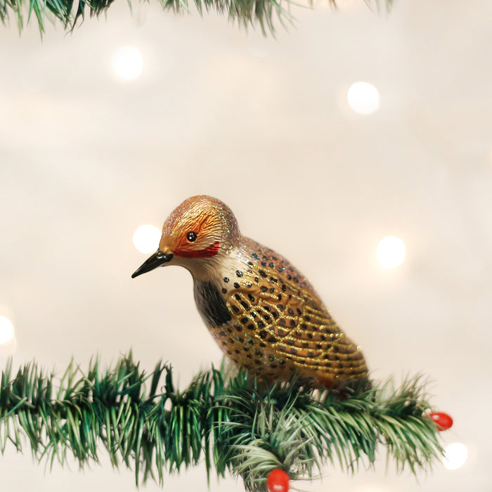 A bird-shaped ornament with brown and gold tones sits on a green artificial pine branch with red berries, against a softly lit, blurred background.