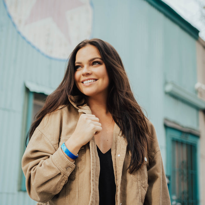 Lifestyle image os someone in front of a building, smiling, and wearing Now Or Never