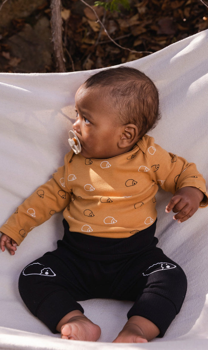 Baby wearing the Deux par Deux organic cotton onesie with brown hedgehog print, view 2
